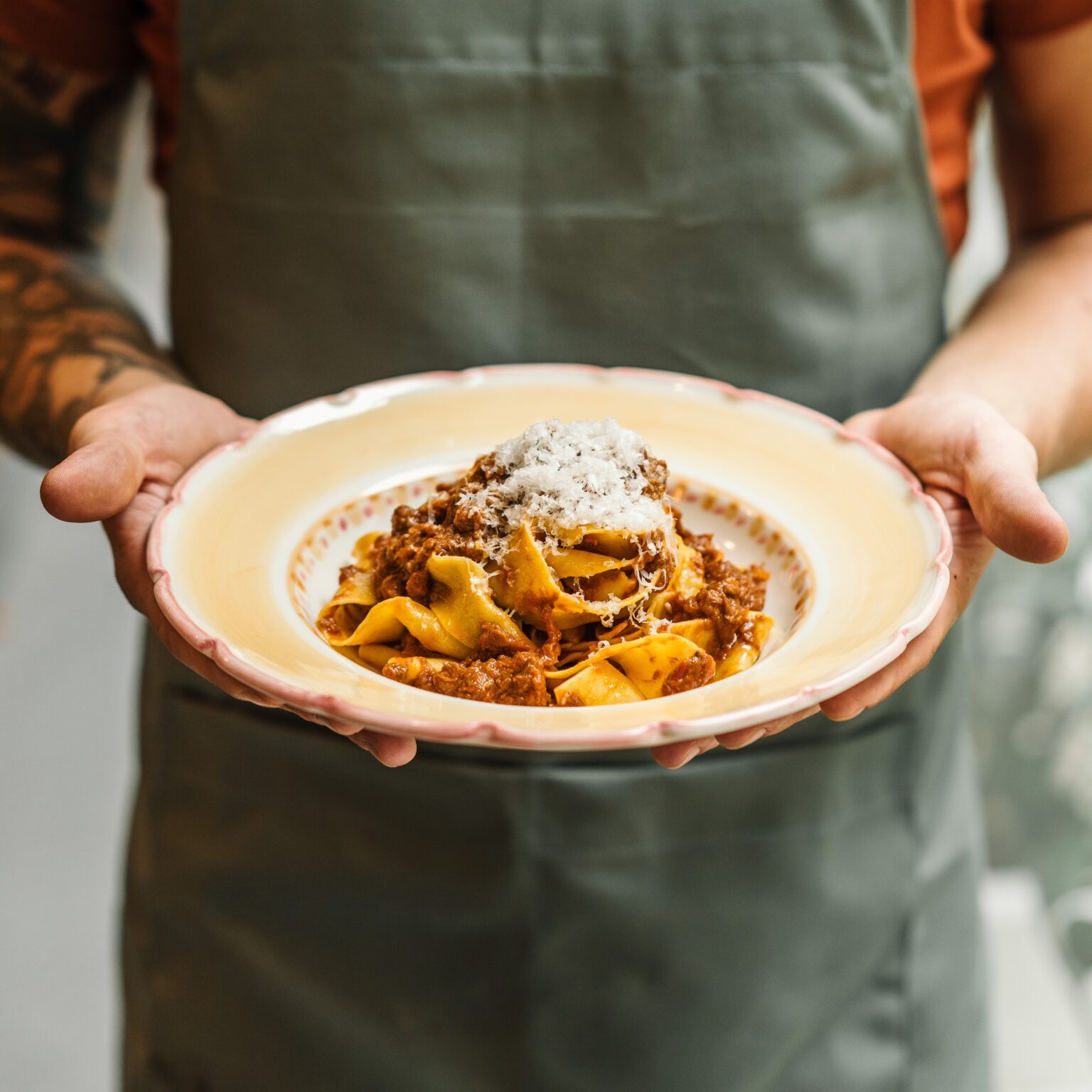 Chef holding a plate of pasta topped with slow-cooked ragu